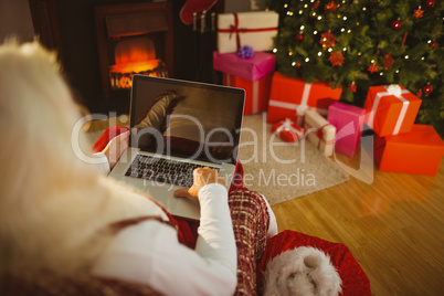 Santa sitting on the armchair and typing on laptop