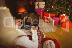 Santa sitting on the armchair and typing on laptop