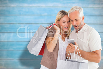 Composite image of happy couple with shopping bags and smartphon