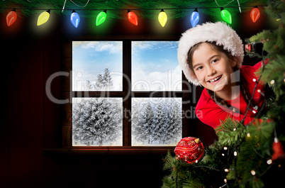 Composite image of festive girl looking from behind christmas tr