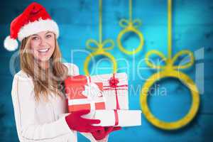 Composite image of festive blonde holding pile of gifts