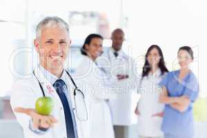 Composite image of mature doctor holding an apple