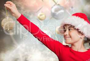 Composite image of festive girl hanging decoration