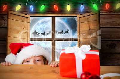 Composite image of festive boy peeking over table