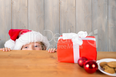 Composite image of festive boy peeking over table