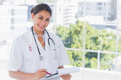 Composite image of doctor smiling and holding clipboard and pen