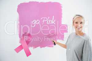 Composite image of happy young woman painting her wall pink