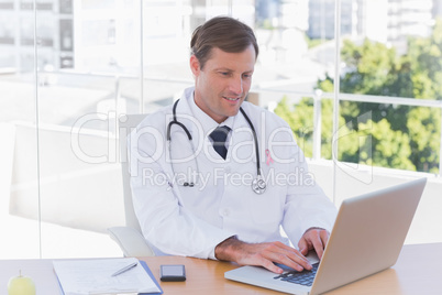 Composite image of happy doctor working on a laptop