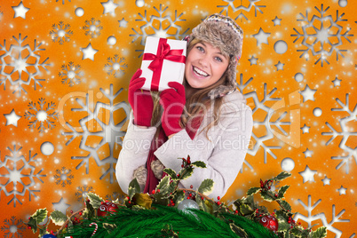 Composite image of happy blonde in winter clothes holding gift