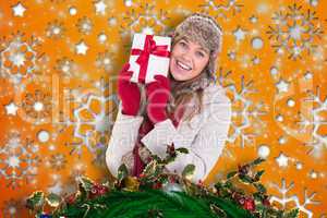 Composite image of happy blonde in winter clothes holding gift