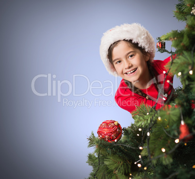 Composite image of festive girl looking from behind christmas tr