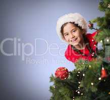 Composite image of festive girl looking from behind christmas tr