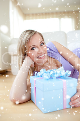 Composite image of bright woman holding a present lying on the f