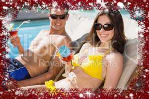 Smiling couple with drinks sitting by swimming pool