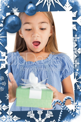 Composite image of surprised little girl holding a wrapped gift