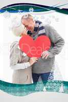 Happy mature couple in winter clothes holding red heart