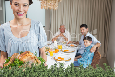 Woman holding chicken roast with family at dining table