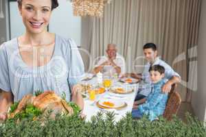 Woman holding chicken roast with family at dining table