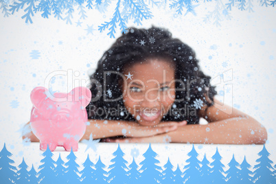 A smiling girl resting her head on her hands with a piggy bank in front of her