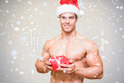 Composite image of shirtless macho man in santa hat holding gift