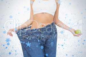 Mid section of slim woman wearing too big jeans holding an apple