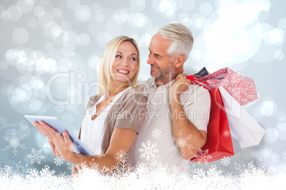 Composite image of happy couple with shopping bags and tablet pc