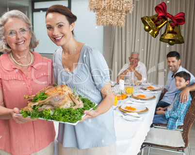 Woman and grandmother holding chicken roast with family at dinin