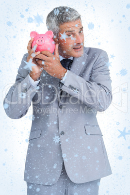 Composite image of curious businessman holding piggy bank