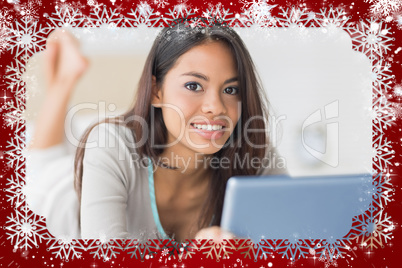 Pretty girl lying on bed using her tablet pc smiling at camera