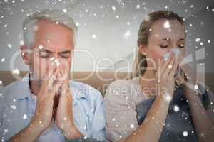 Composite image of sick couple blowing their noses sitting on th