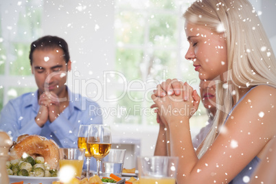 Composite image of woman saying grace with family before dinner