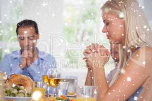 Composite image of woman saying grace with family before dinner