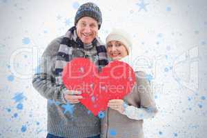 Happy mature couple in winter clothes holding red heart