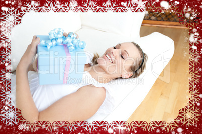 Charming blond woman holding a present lying on a sofa