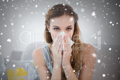 Sick young woman sitting on sofa blowing her nose