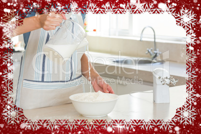 Mid section of woman pouring milk into dough at kitchen