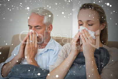 Composite image of sick couple blowing their noses sitting on th