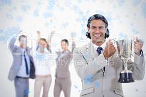 Close up of a man dressed in a suit smiling and holding a cup with people cheerin