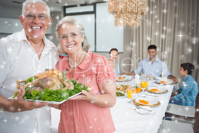 Composite image of grandparents holding chicken roast with famil