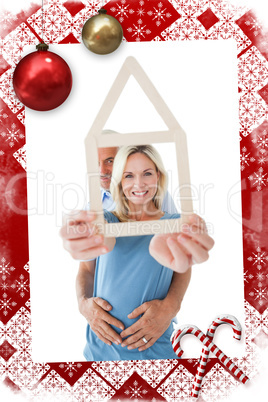 Composite image of happy couple holding house outline