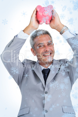 Composite image of cheerful businessman holding piggy bank above his head
