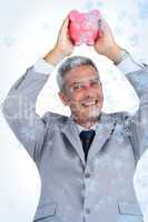 Composite image of cheerful businessman holding piggy bank above his head