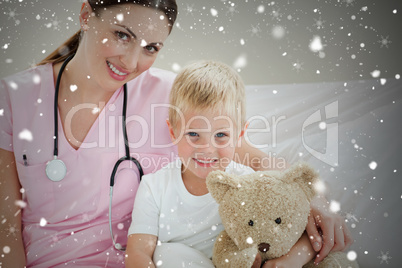 Smiling little boy holding a teddy bear on a hospital bed