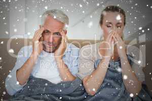 Composite image of sick couple sitting on the couch under a blan
