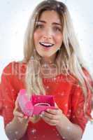 Composite image of surprised blonde woman opening gift