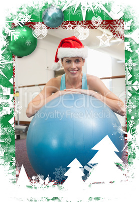 Fit smiling brunette in santa hat leaning on exercise ball