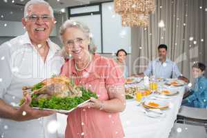 Composite image of grandparents holding chicken roast with famil
