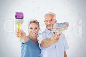 Happy couple holding paintbrushes smiling at camera
