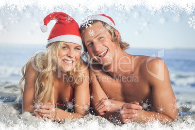 Composite image of couple lying on beach wearing christmas hats