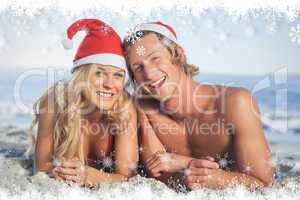 Composite image of couple lying on beach wearing christmas hats